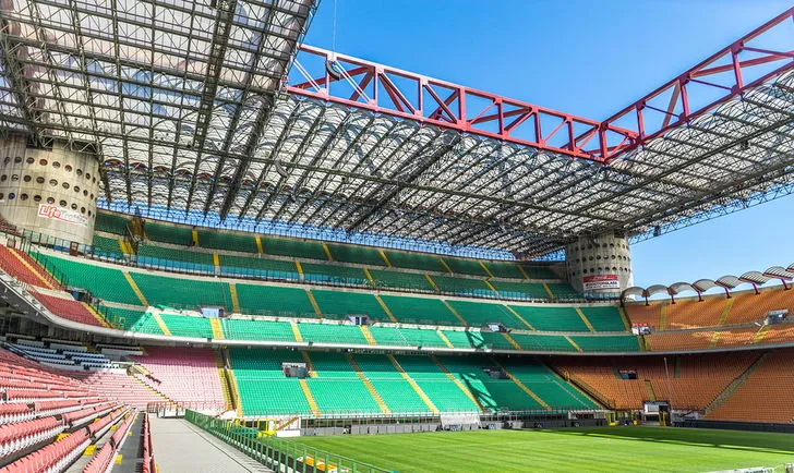 Không gian bên trong sân San Siro nhìn từ khán đài, cho thấy hàng ghế khán giả, cấu trúc mái vòm và chất lượng mặt sân