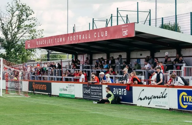 Không khí trận đấu tại St James Park Brackley, cho thấy sự tương tác giữa cầu thủ và cổ động viên
